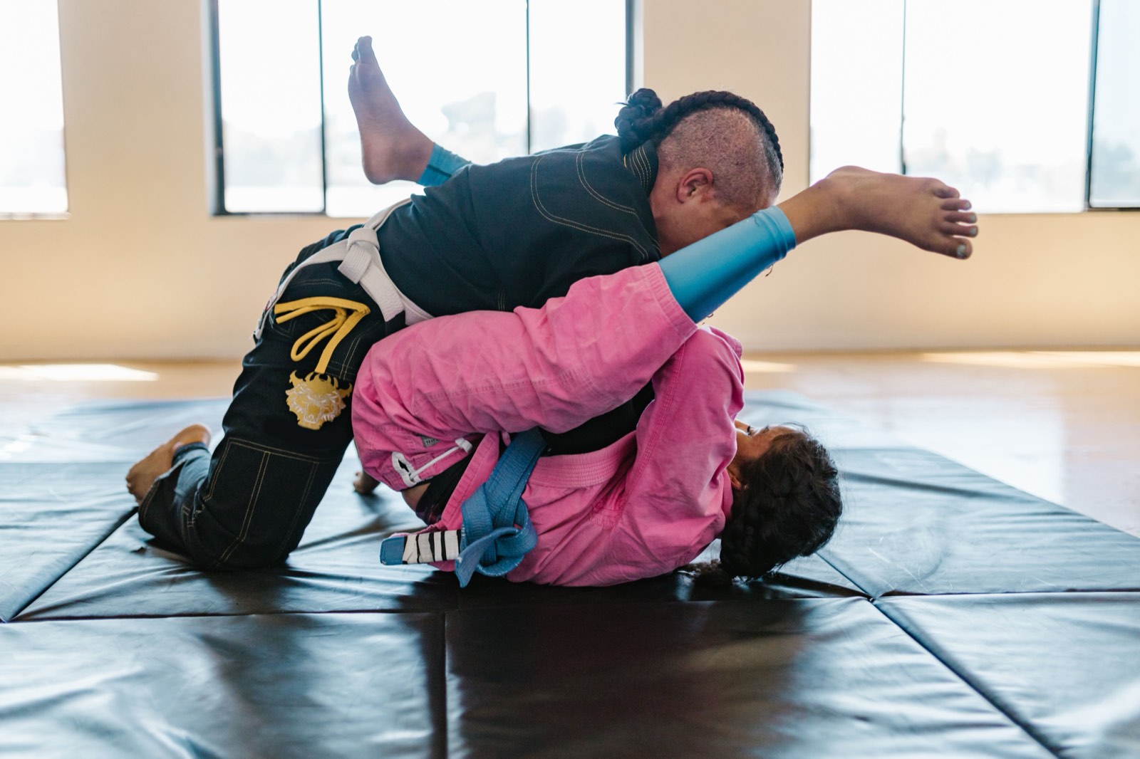 Two BJJ athletes training in pink and black gis on academy mats