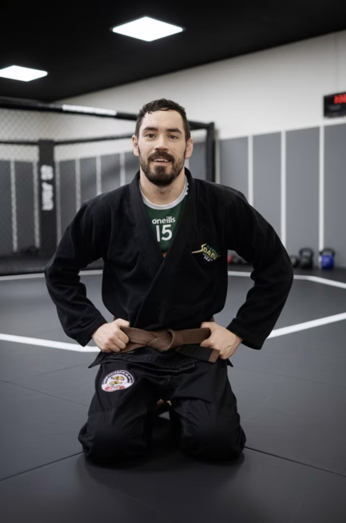 Brian O'Connor, GrapplerHQ founder, kneeling in a black gi and BJJ brown belt