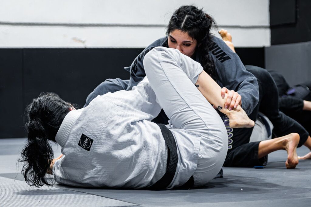Two Brazilian jiu-jitsu practitioners in gis at close quarters on the mat, one controlling the other's arm