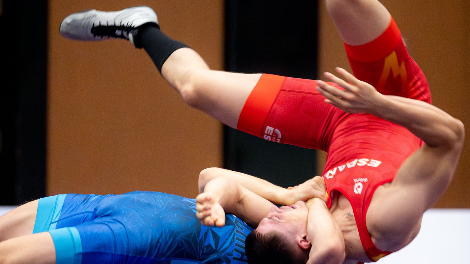 Freestyle wrestler in red being taken over in a high-arching throw during a competition match