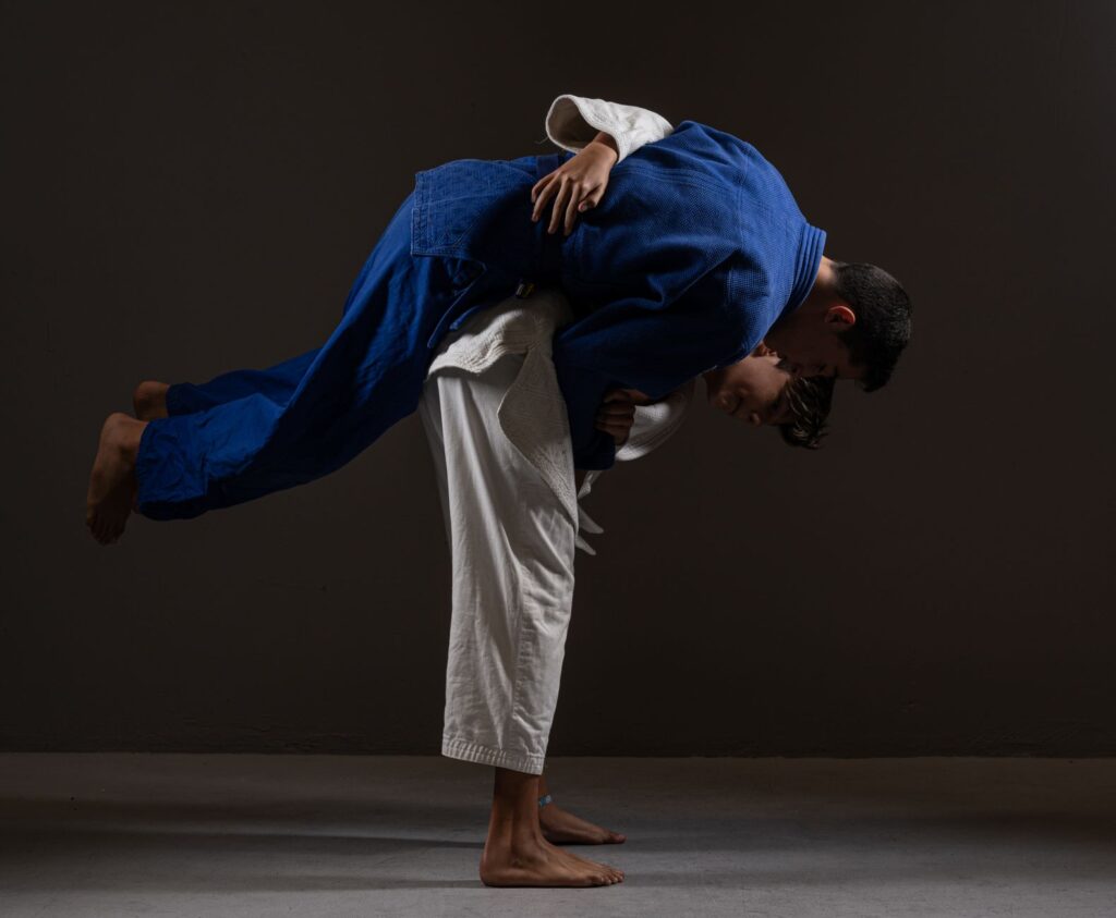 One judoka loading another across the hips in a judo hip throw against a dark background