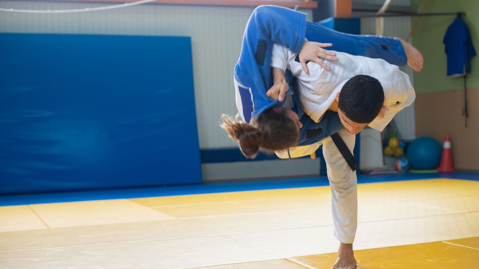 Judoka in a white gi throwing a partner in a blue gi with a hip throw during training on tatami mats