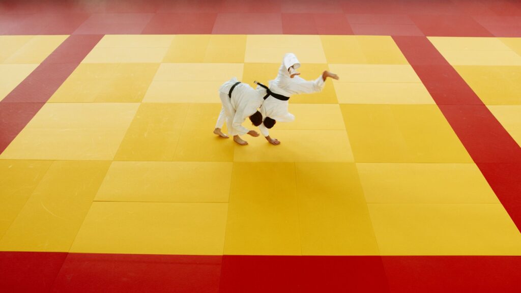 Two judoka in white gis and black belts executing a throw on a competition tatami