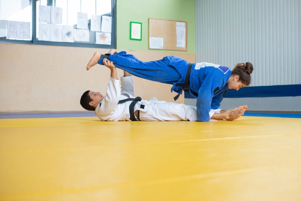 Adult gi athletes practicing grips and leg positioning on a mat
