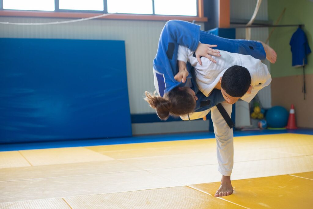Jacketed grappler executing a throw on a mat, the shared throwing base of sambo and judo