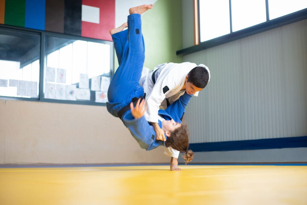 Judoka throwing a partner in a blue gi during judo practice on a tatami mat
