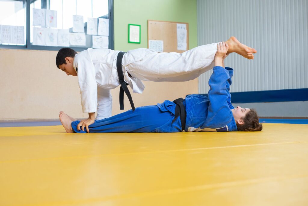 Adult gi athletes practicing leg positioning from the ground