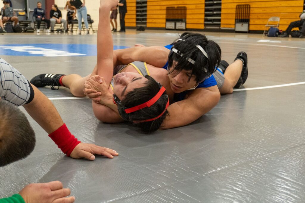 Two high school wrestlers competing on a wrestling mat, one riding the other