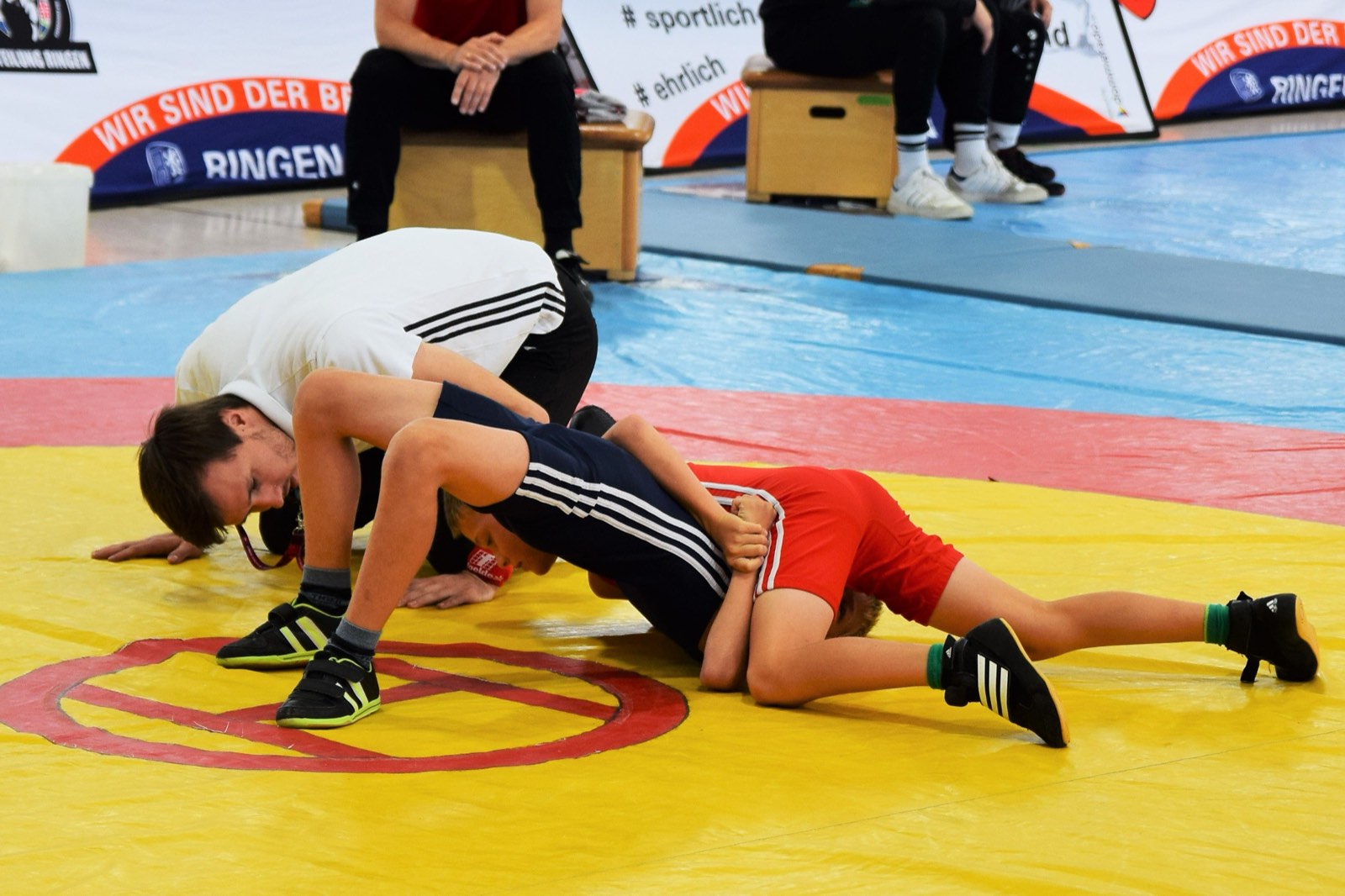 Young wrestlers competing on the mat with a referee officiating