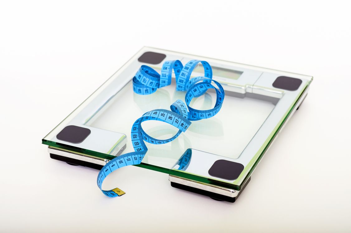 Clear glass digital weighing scale with a blue measuring tape on top.